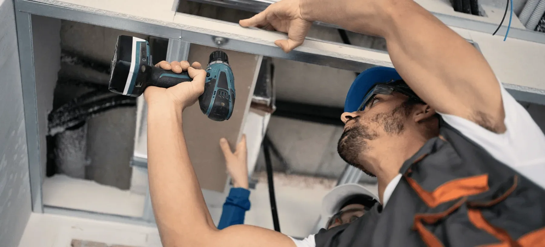 A technician drilling into a ceiling duct.