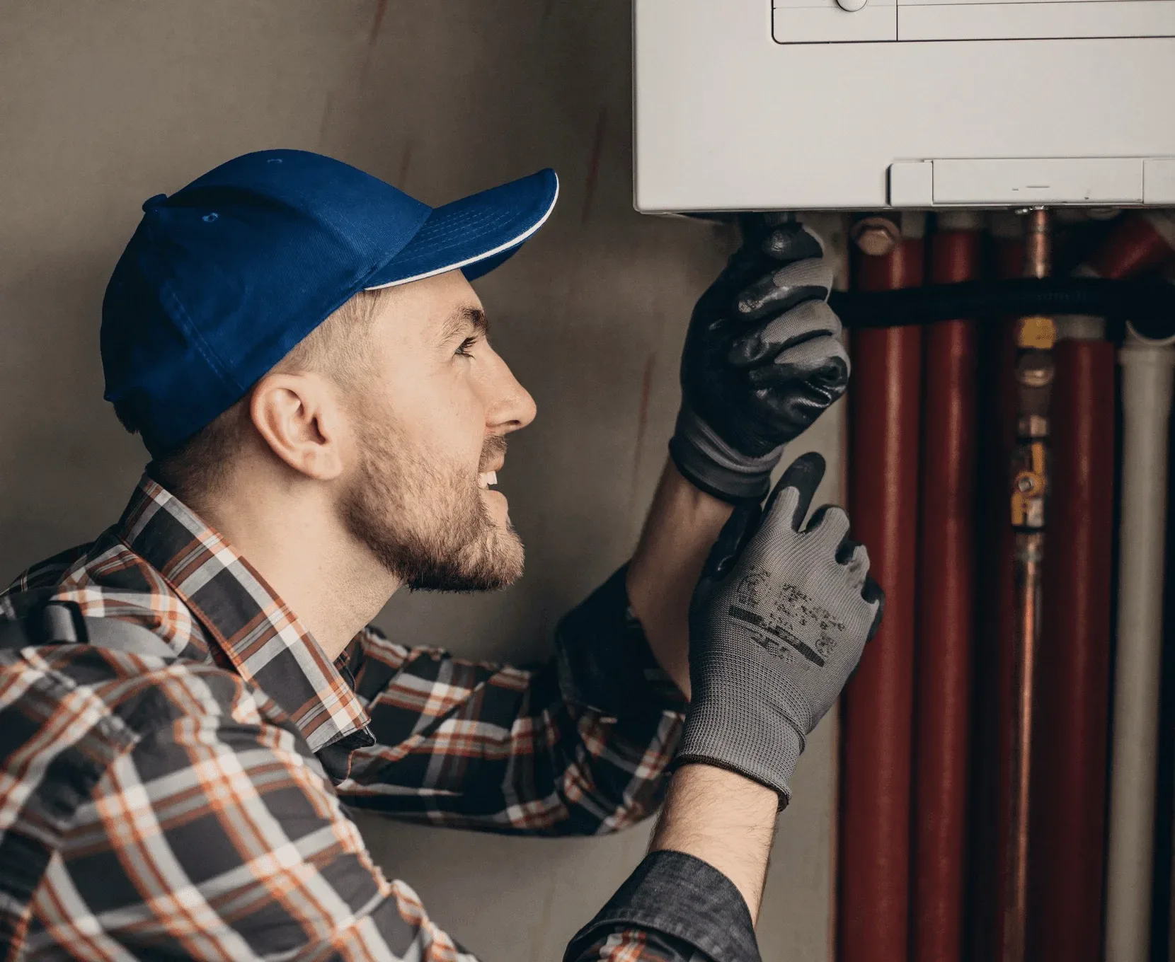A technician in a blue cap working at red pipes.