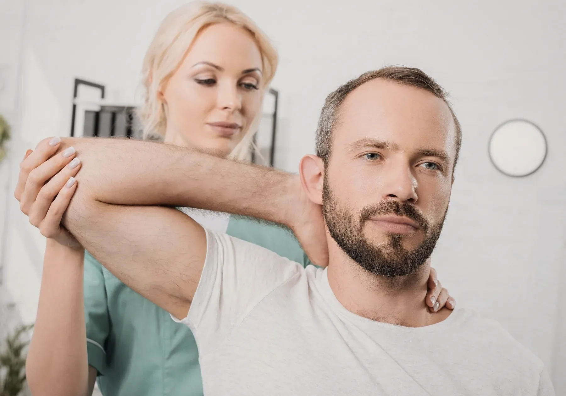 A physiotherapist stretching a man's arm across his chest.