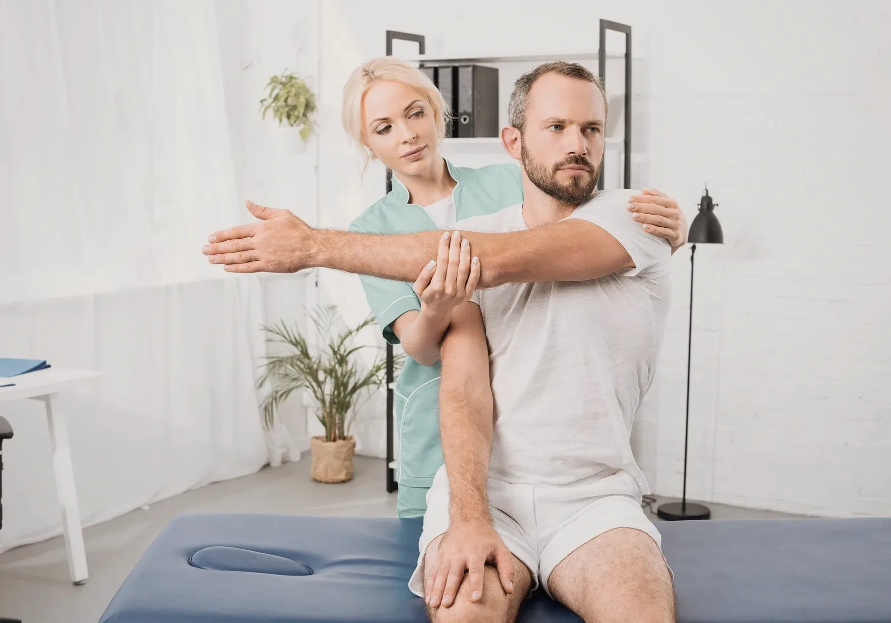 A physiotherapist guiding a man's arm behind his head.