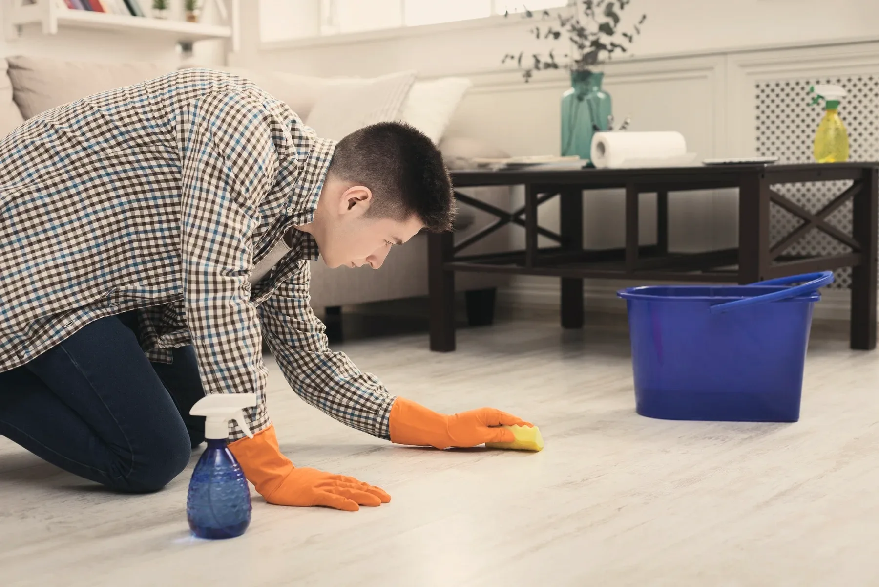 A cleaner on their knees wiping a wooden floor, a blue bucket beside.