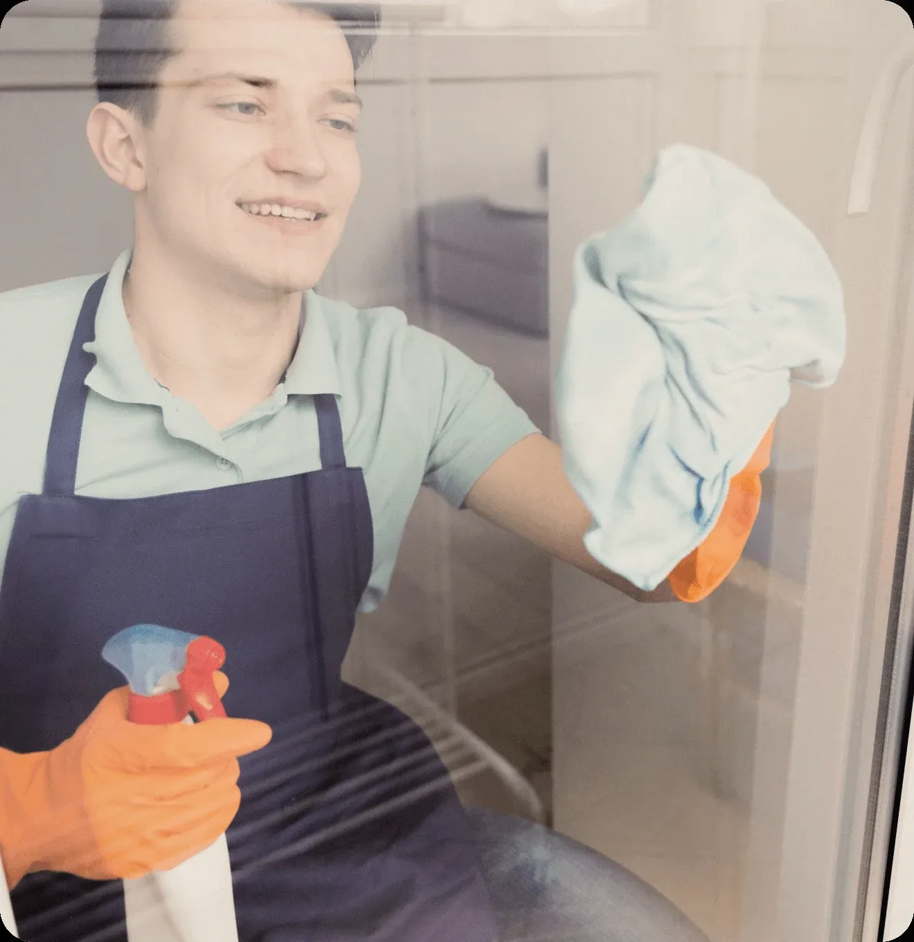 A cleaner in a blue apron wiping a window.