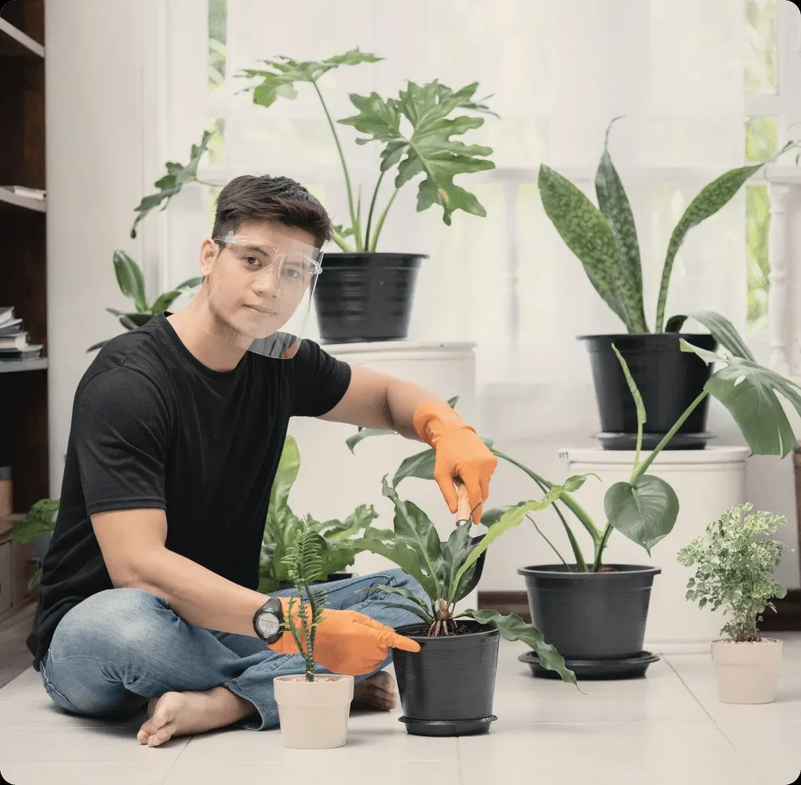 A cleaner in orange gloves among potted plants.