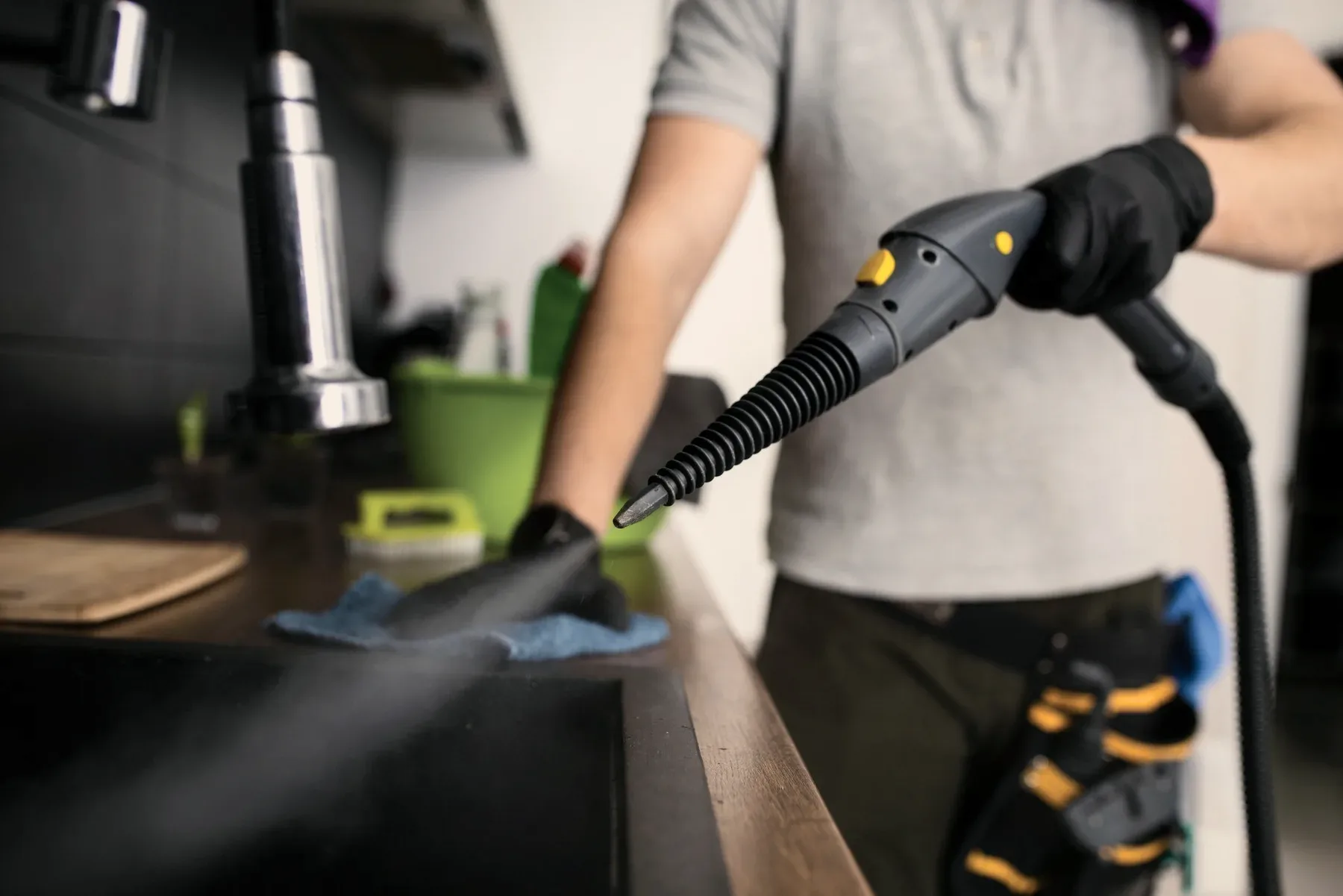 Gloved hands with a steam cleaner at a counter.