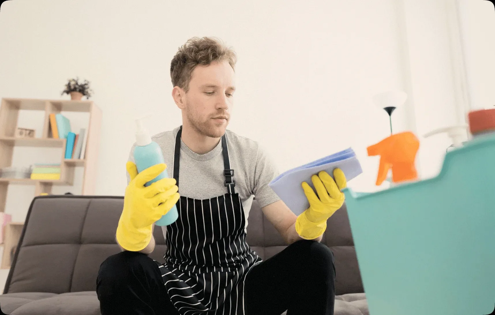 A cleaner in a striped apron sitting with a bottle and a sponge.