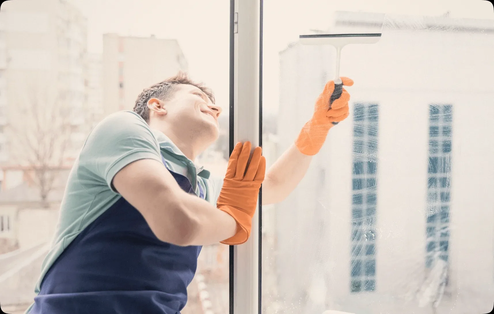 A cleaner in orange gloves squeegeeing a window.