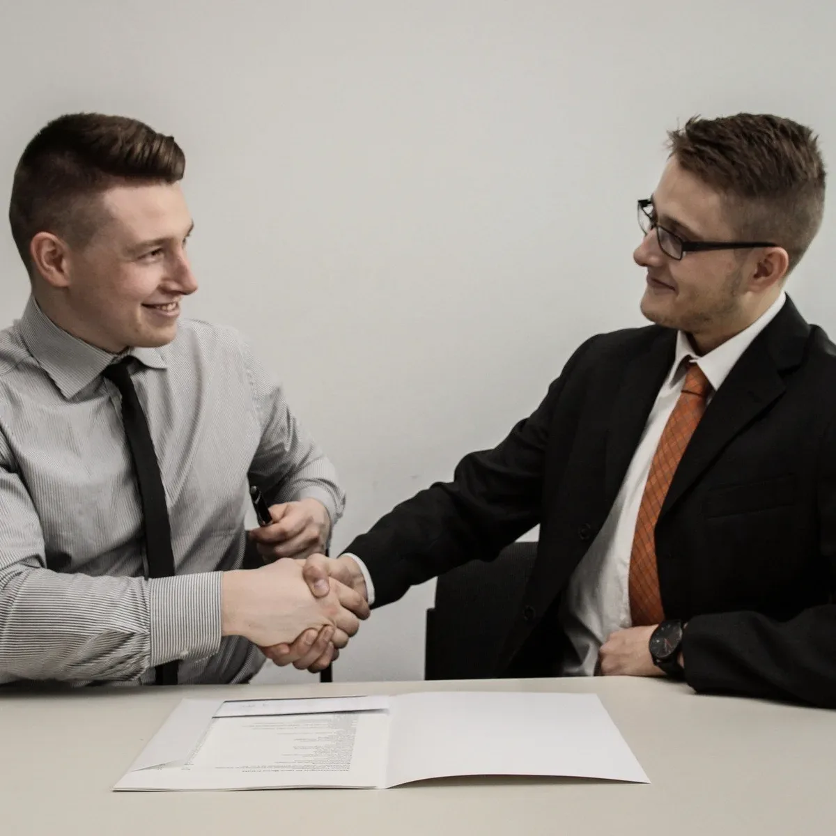 Two men in shirts and ties laughing at a desk.