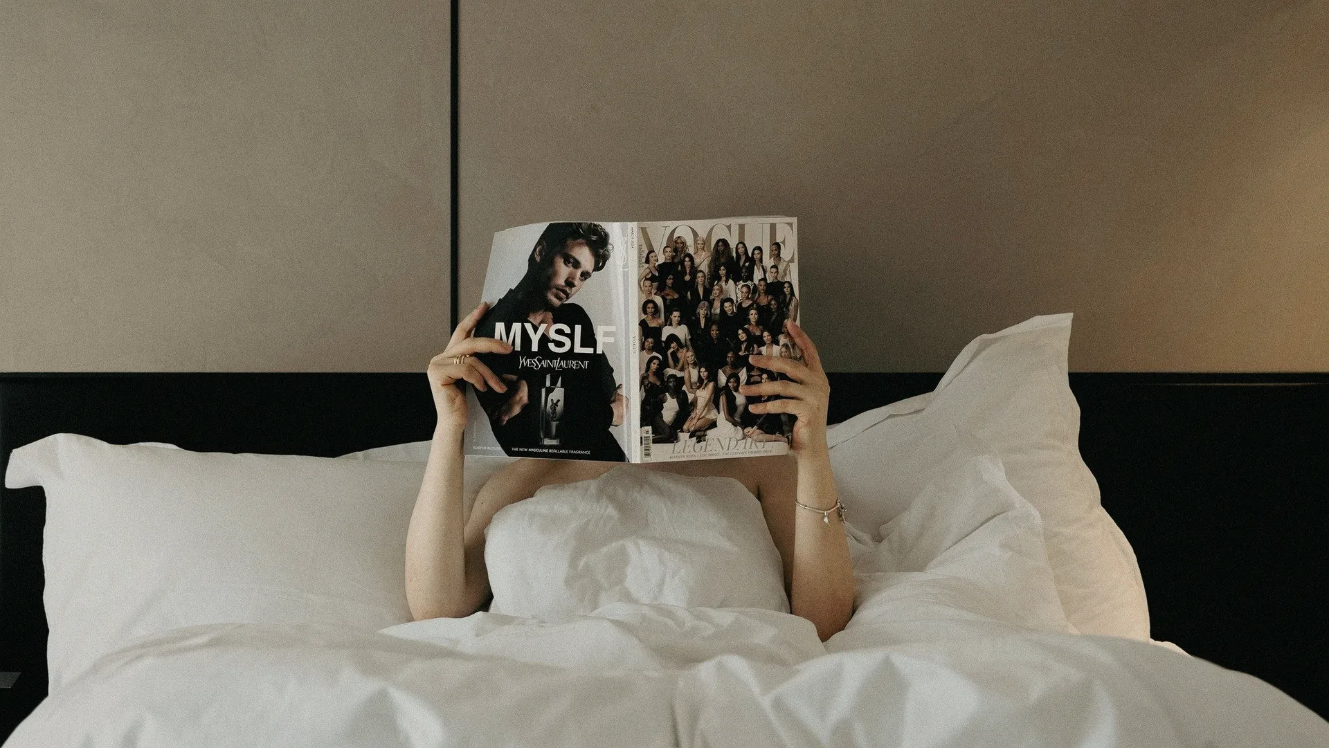 A person in bed holding a magazine over their face.
