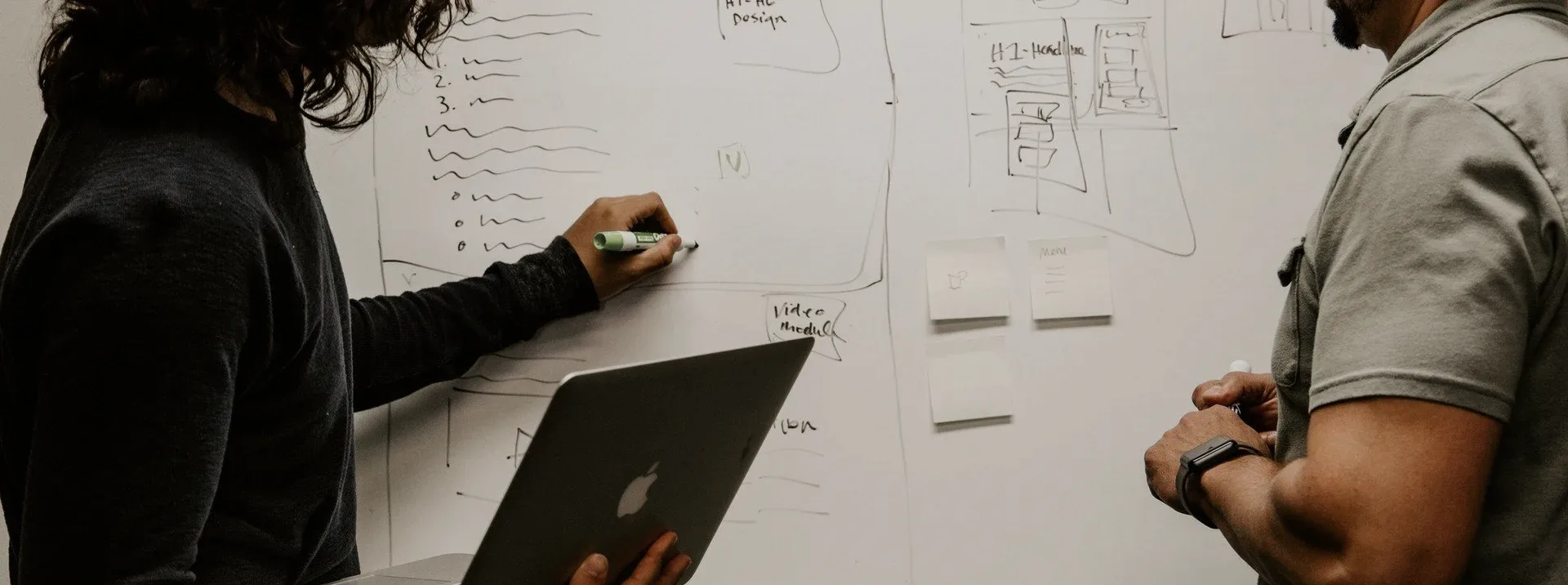 Two people at a whiteboard with a laptop.