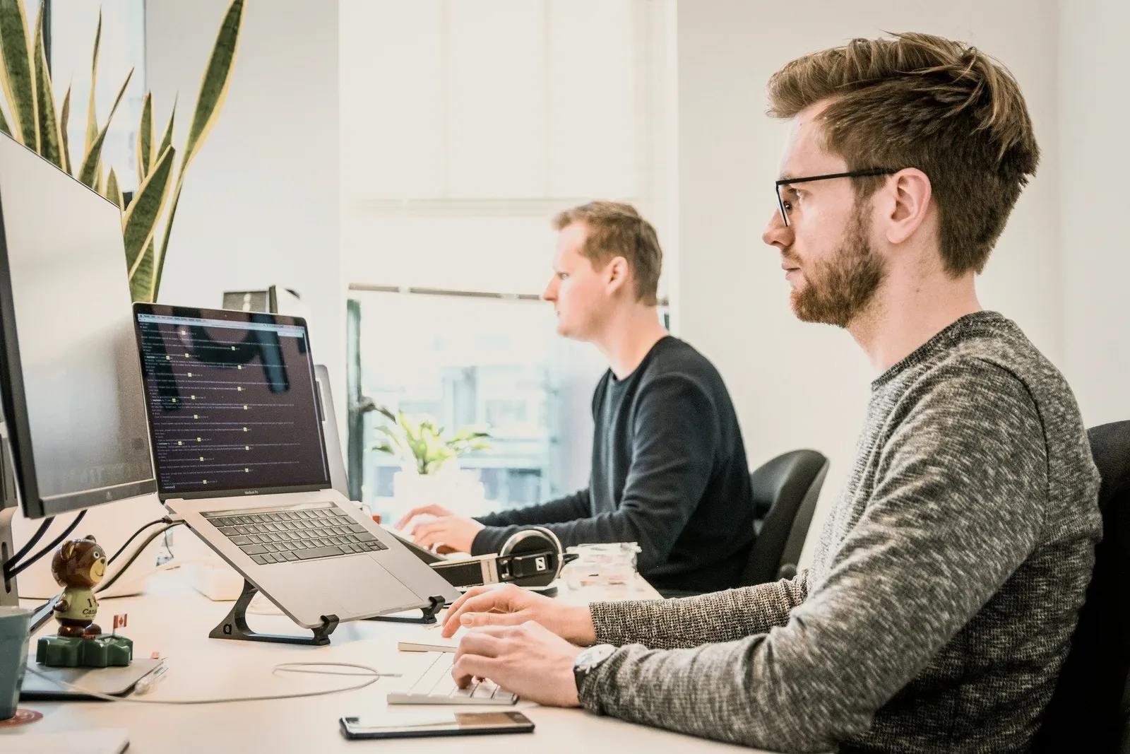 Two people working at laptops by a window.