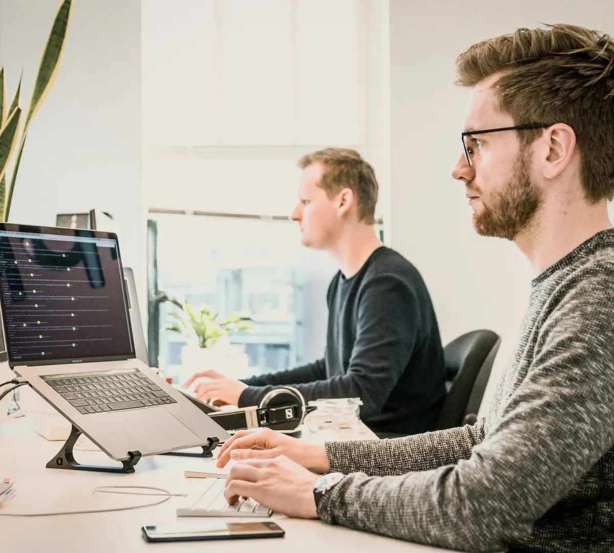 Two people at laptops by a window.