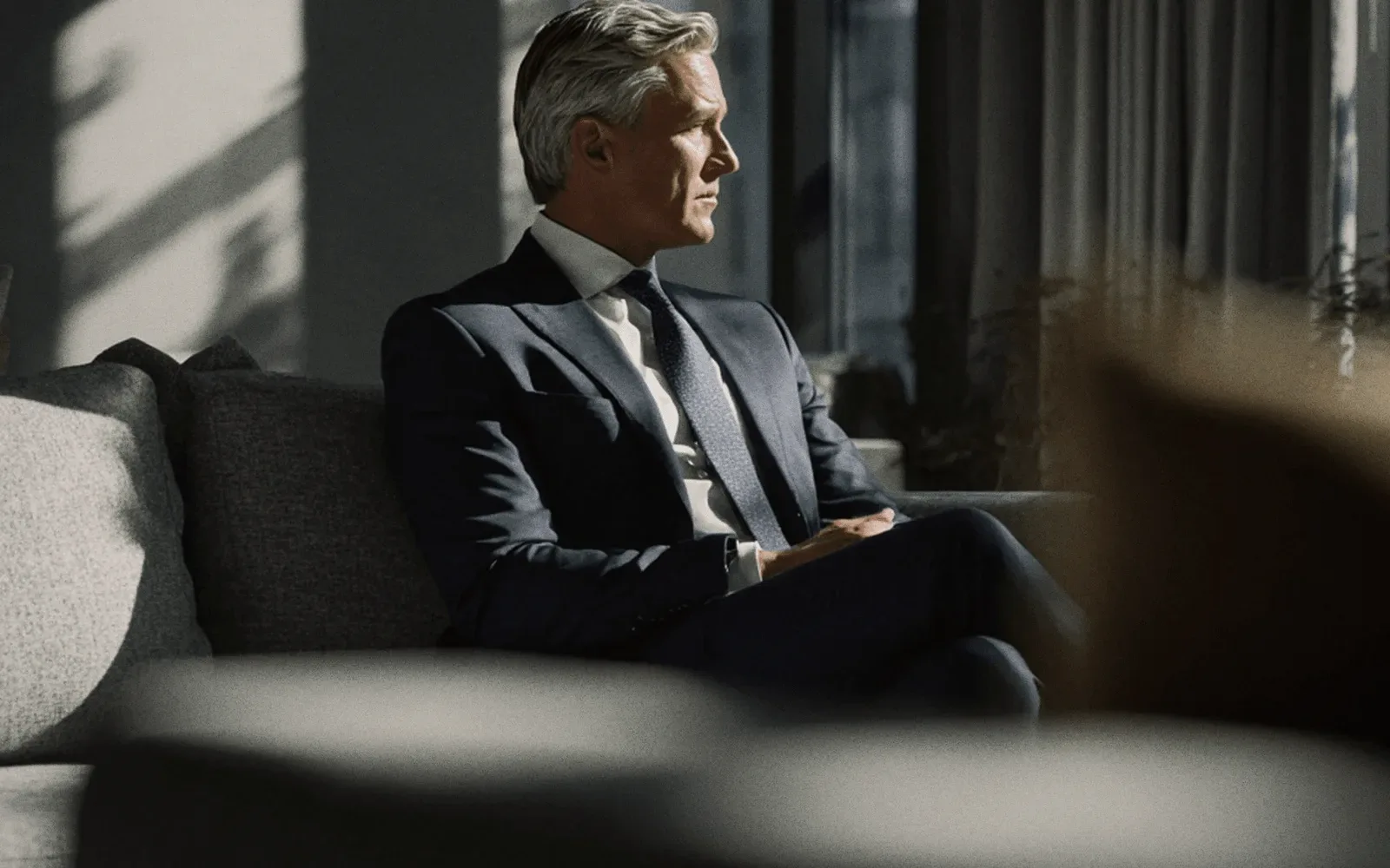 A man in a navy suit on a sofa.