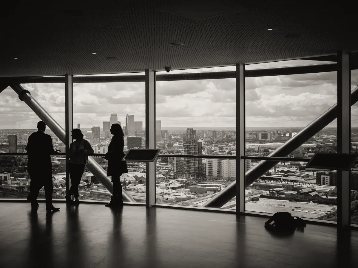People in silhouette inside a glass building.