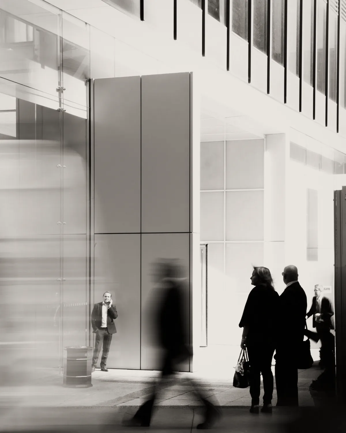 People walking through a glass lobby, in grey.