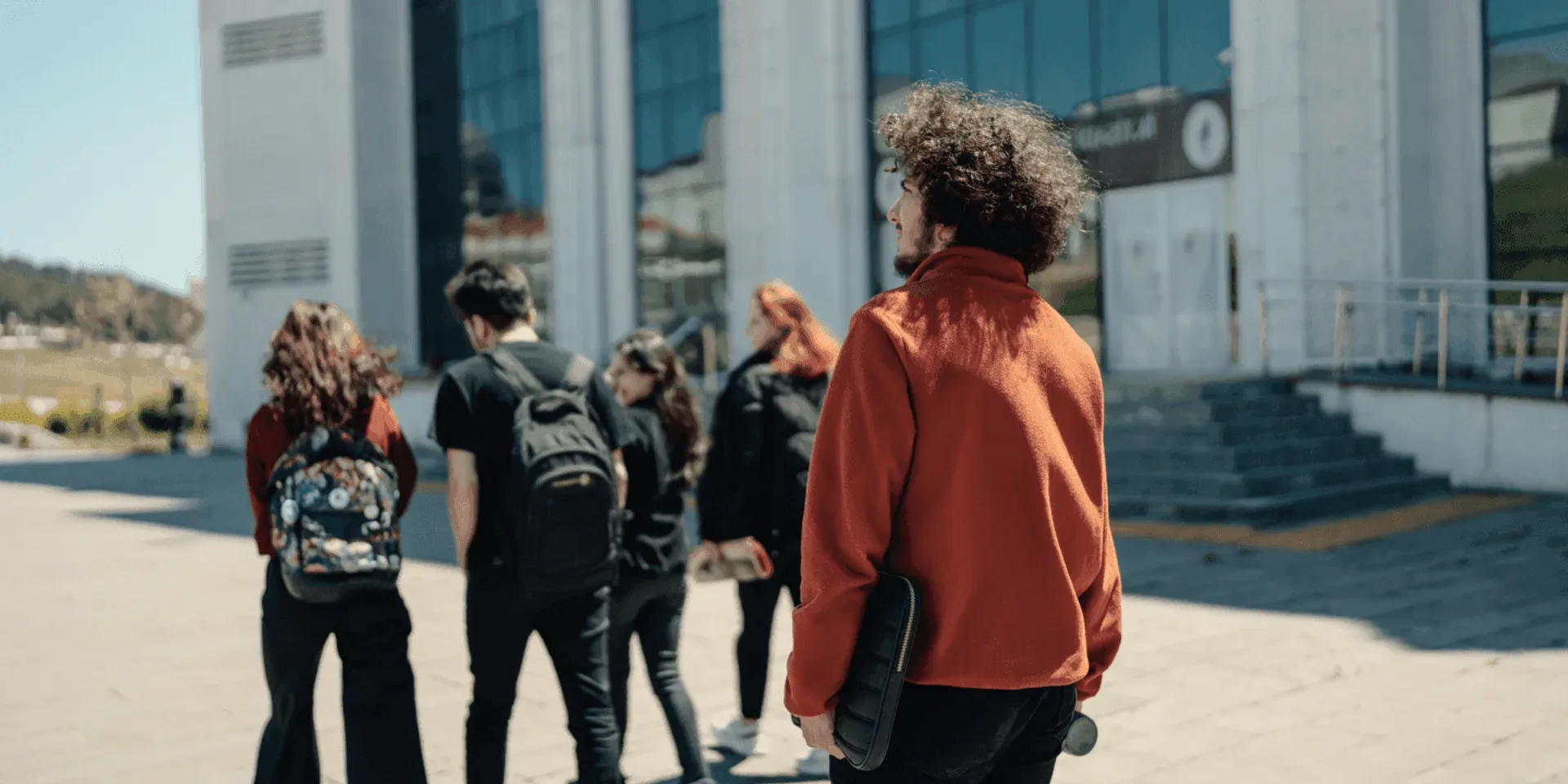 Students walking away across a campus square, one in a red hoodie.