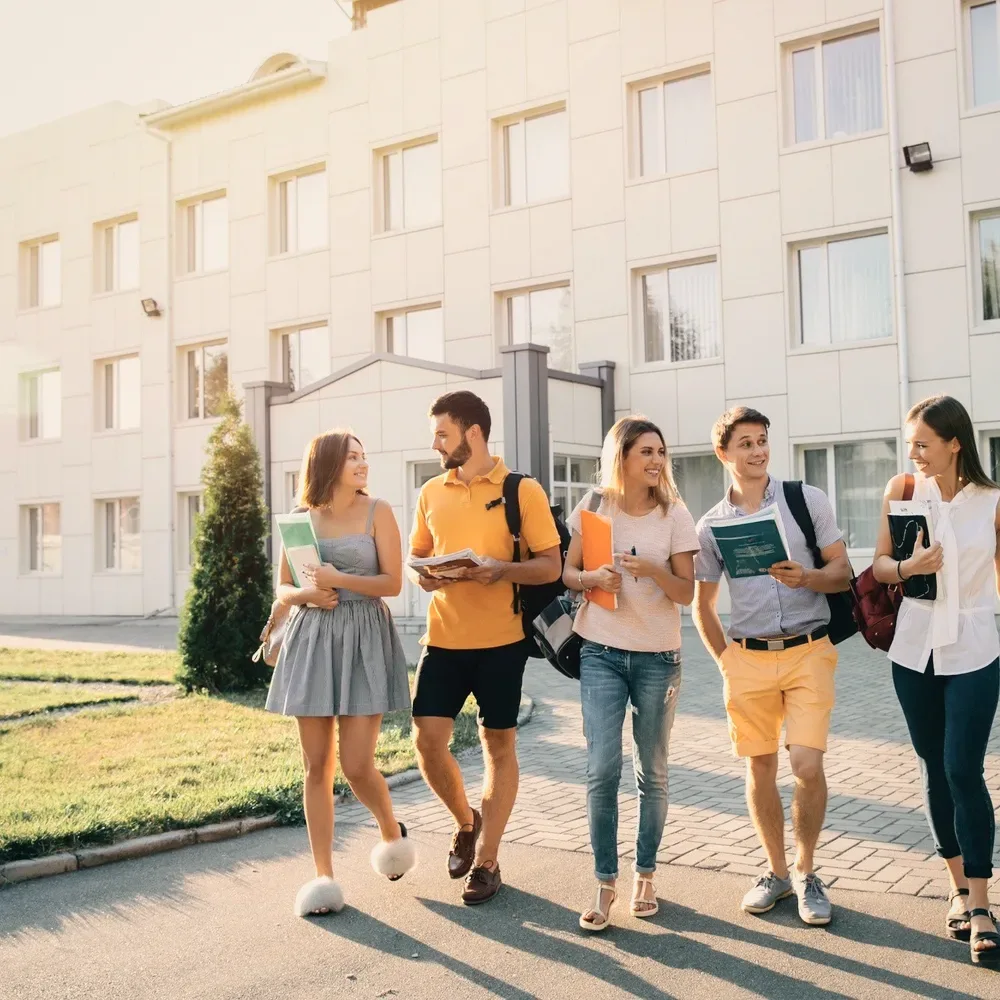Five students walking past a white building.
