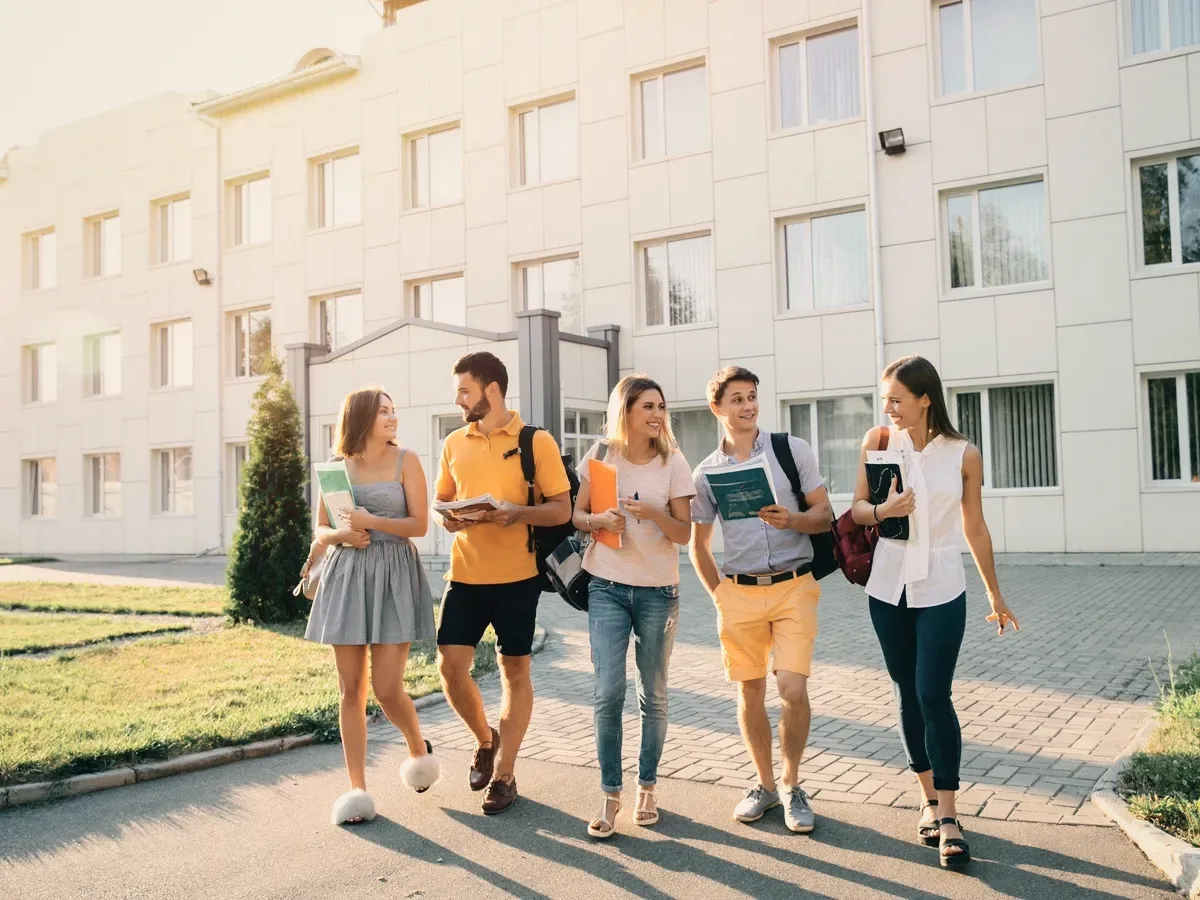 Five students walking past a white building.