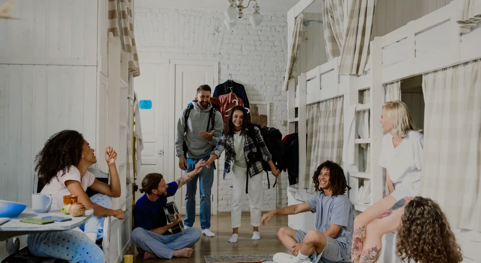 Backpackers greeting each other in a dorm with white bunk beds.