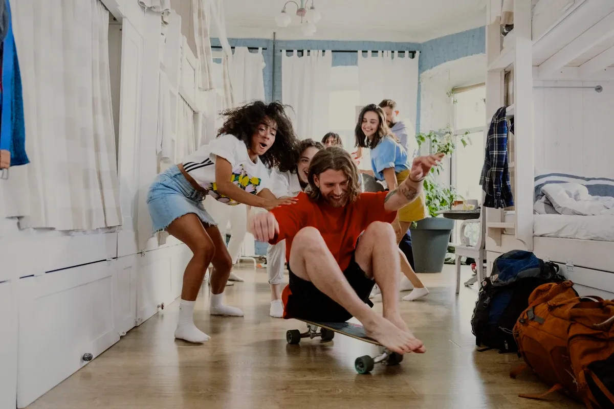 Friends playing with a skateboard in a dorm.