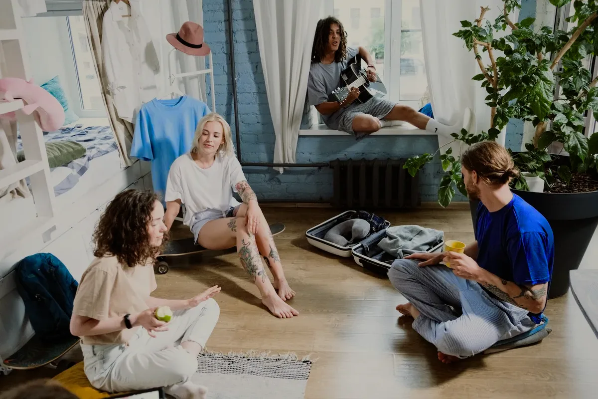 Friends sitting on the floor of a sunny room around a suitcase.