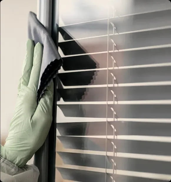 A gloved hand wiping a window blind.