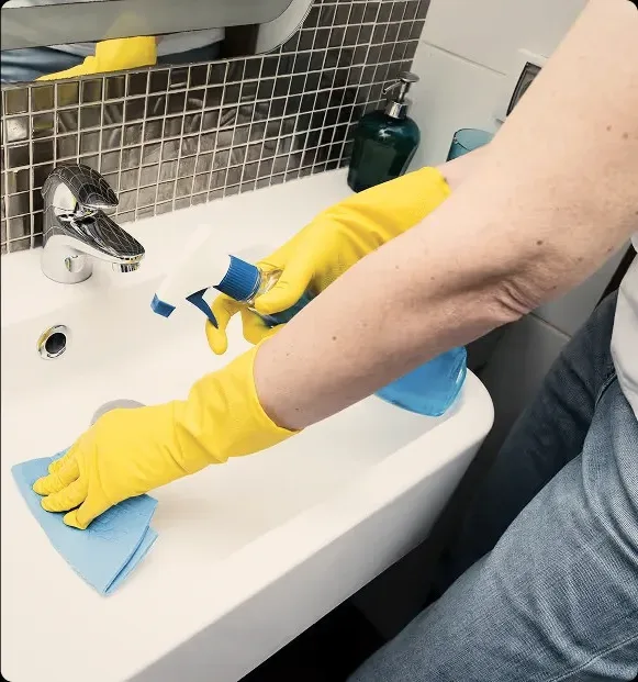 Yellow rubber gloves cleaning a bathroom sink.