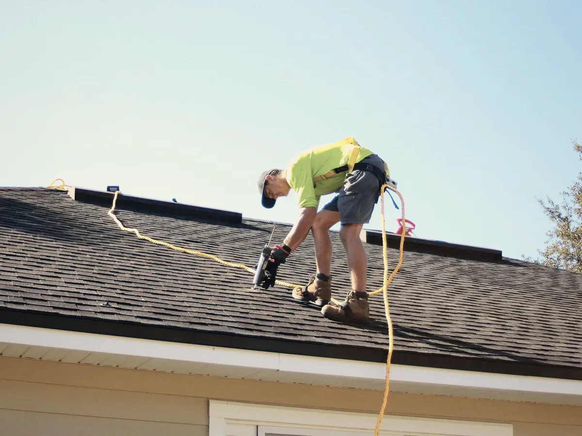 A roofer with a nail gun on shingles.