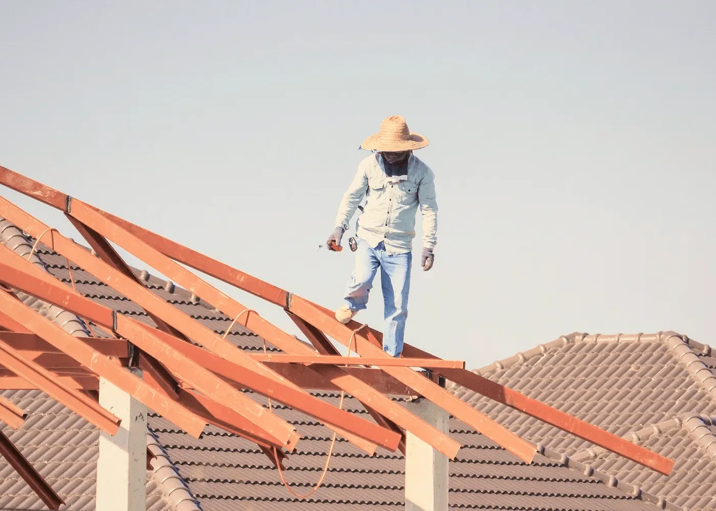 A roofer in a straw hat on red rafters.