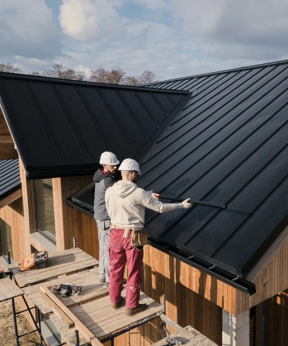 Two roofers on a dark metal roof.