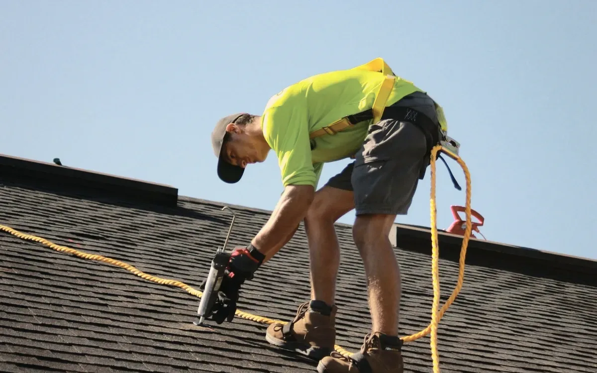 A roofer in a yellow shirt on a shingle roof.