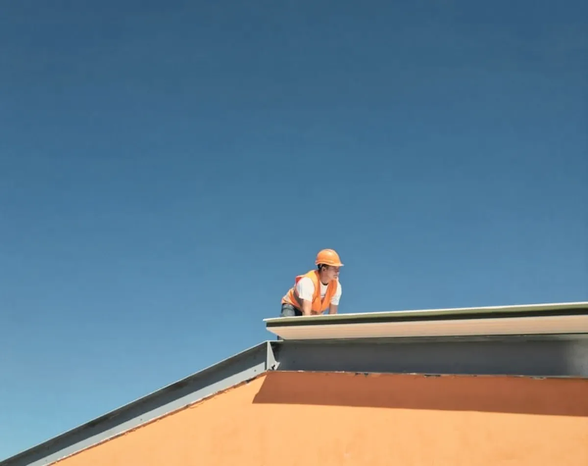 A roofer in orange on a roof against blue sky.