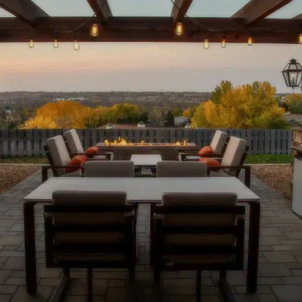 An outdoor terrace with cushioned chairs around a fire pit at dusk.