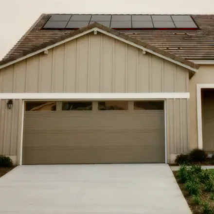 A house front with a closed garage door and solar panels on the roof.