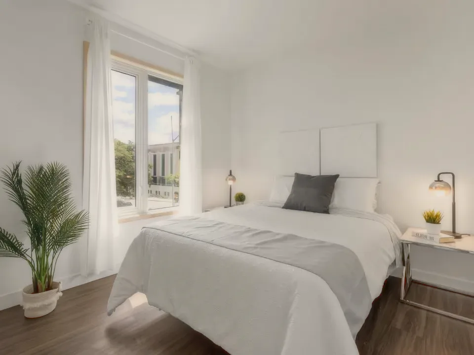 A bright bedroom with grey and white linen and a bedside lamp.