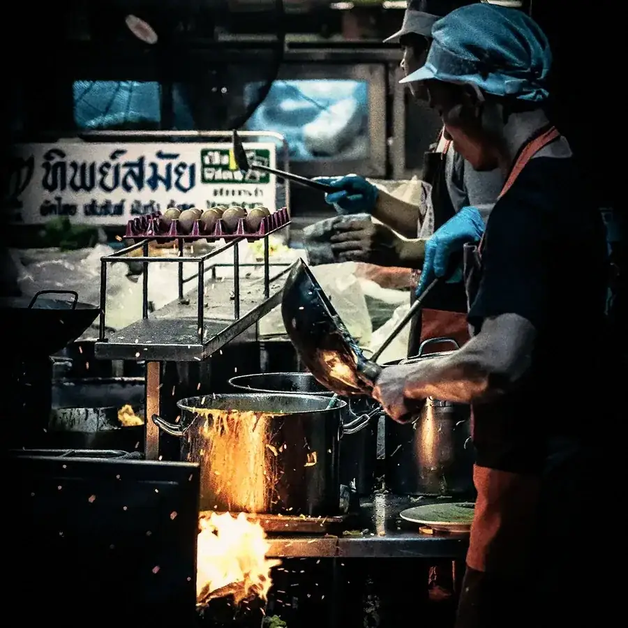 A cook tossing a wok over the fire at a night street-food stall.