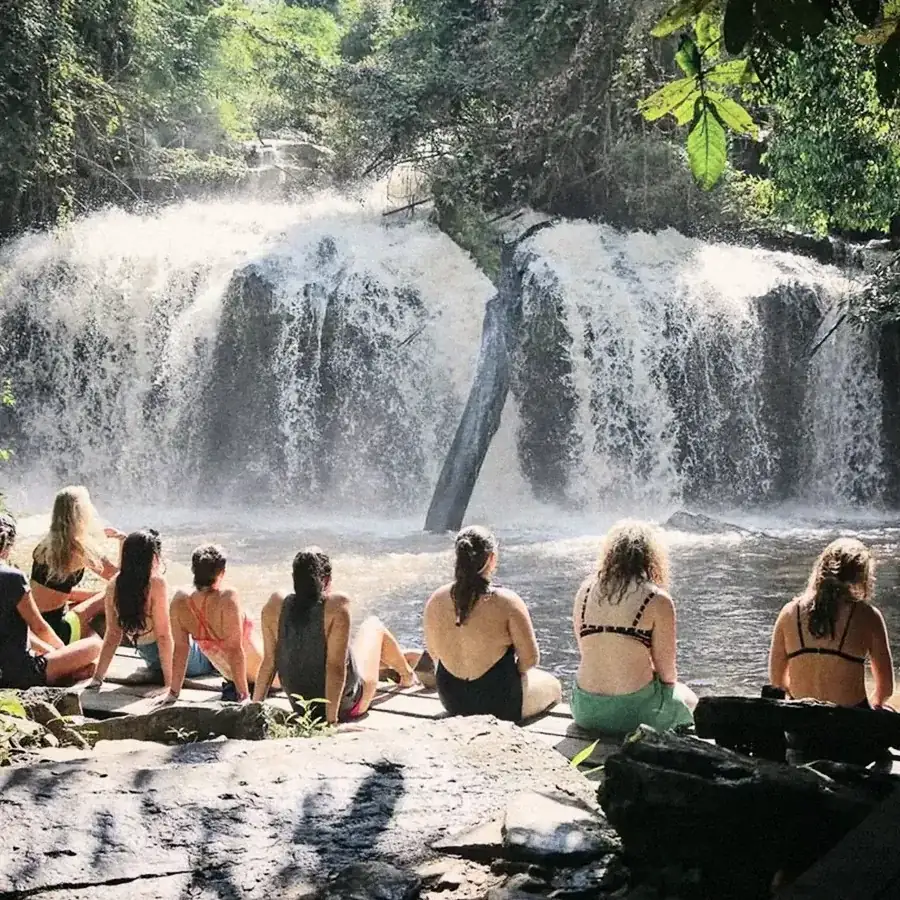 Travellers sitting on the rocks in front of a waterfall.