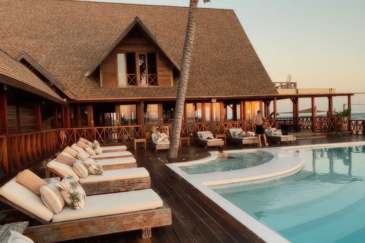 A wooden villa with a pool and loungers at dusk.
