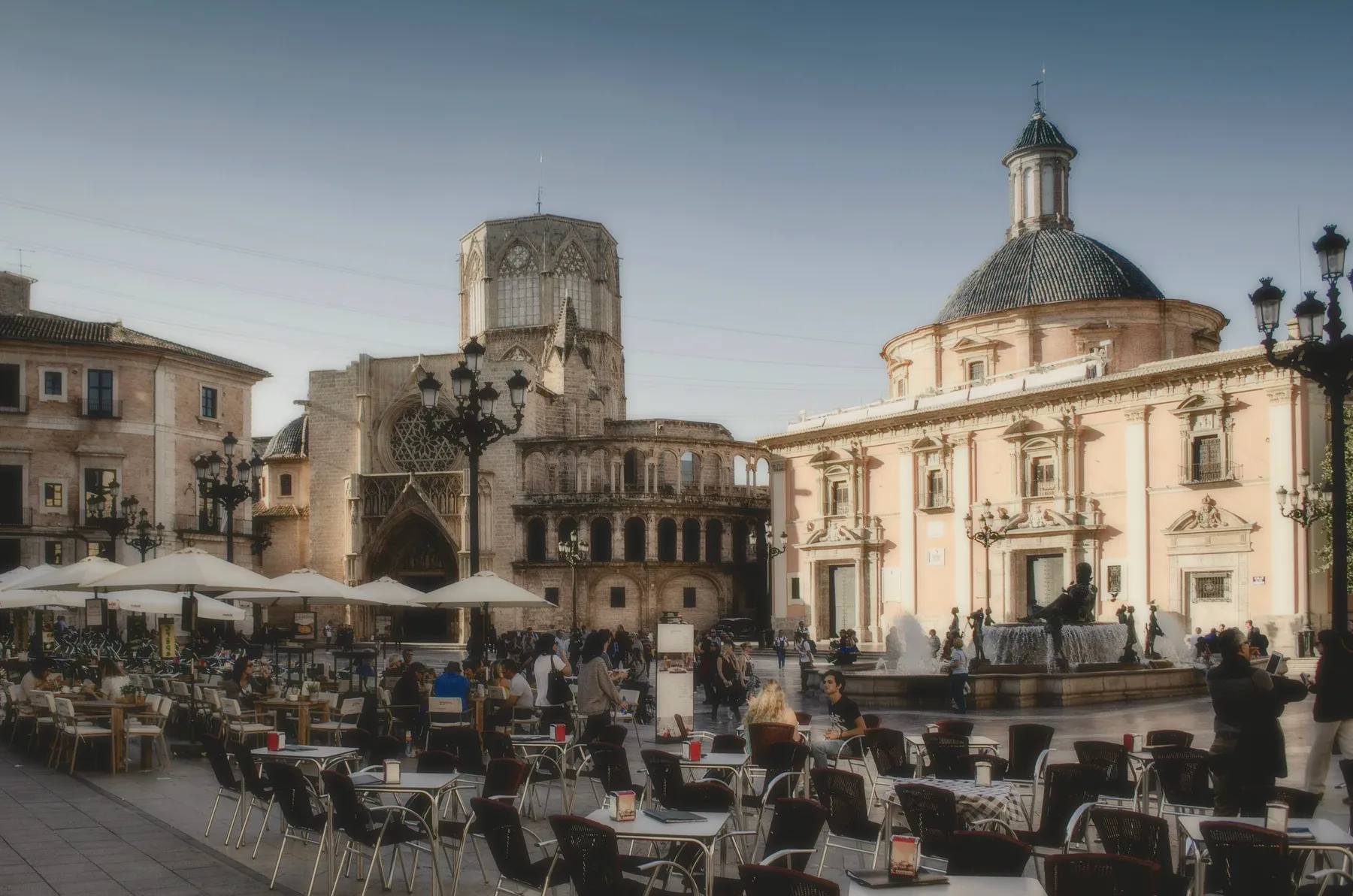 A city square with a cathedral and cafe tables.