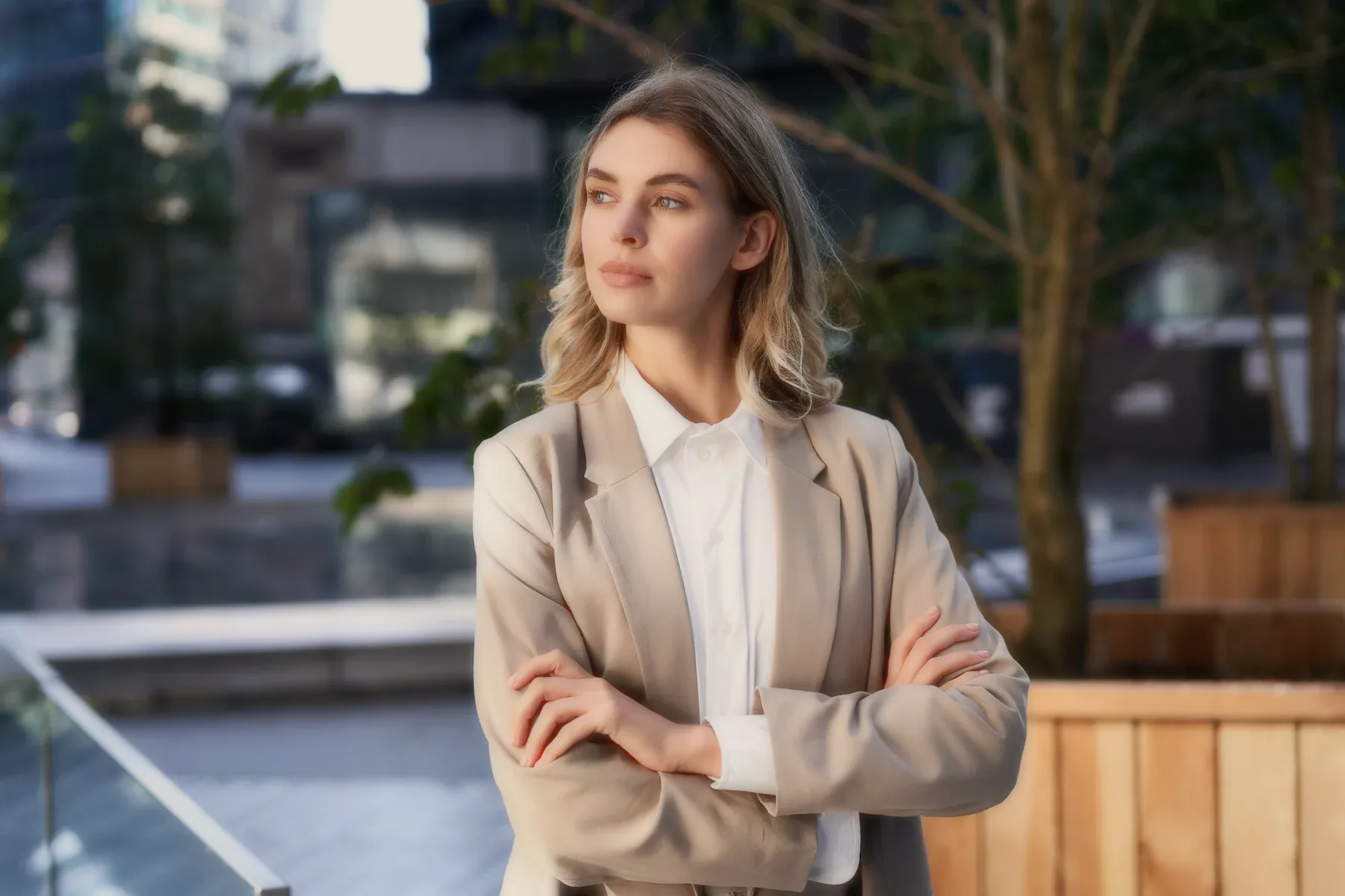 A woman in a blazer outdoors, arms crossed.