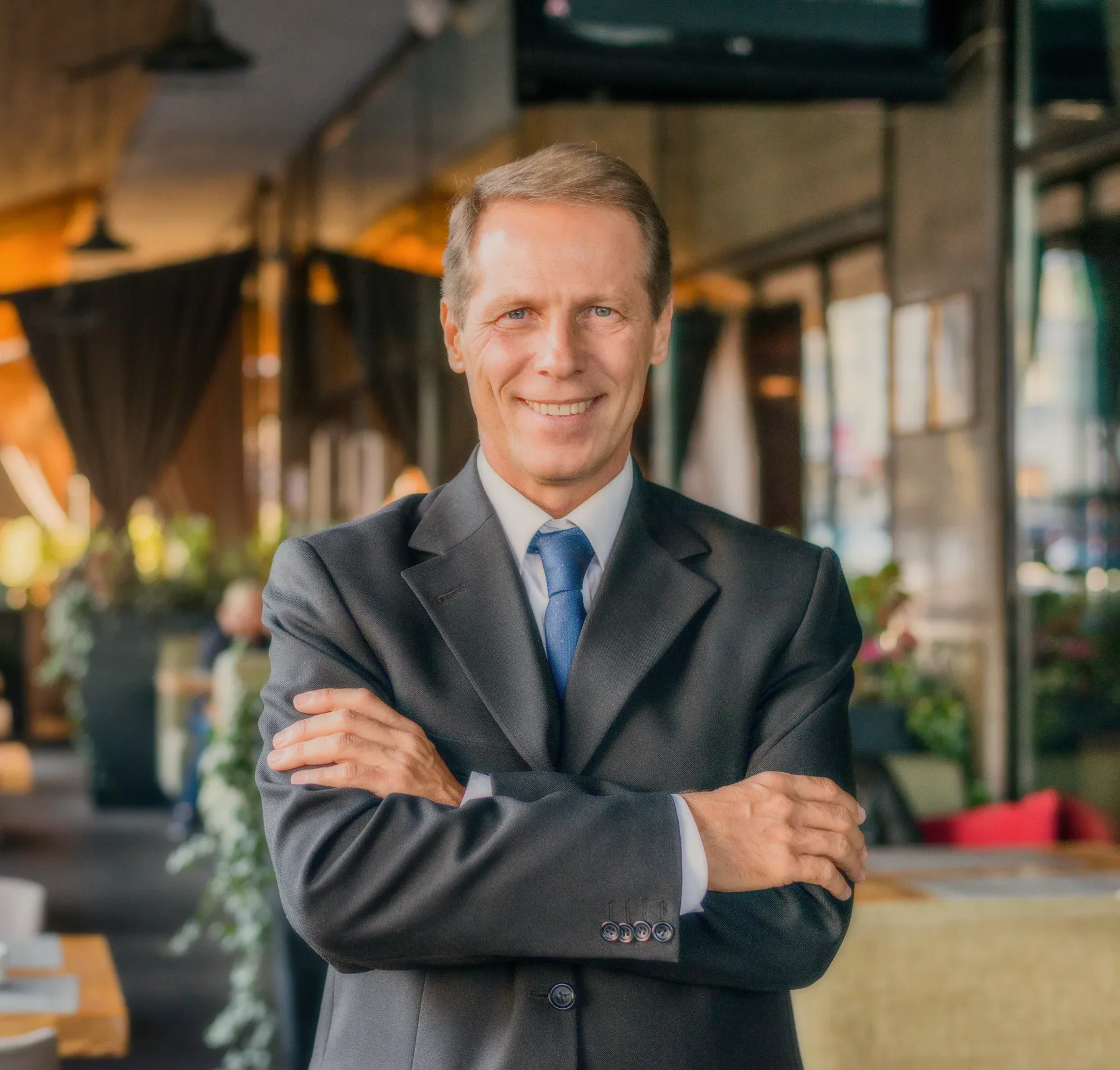 A man in a suit with arms crossed in a lobby.