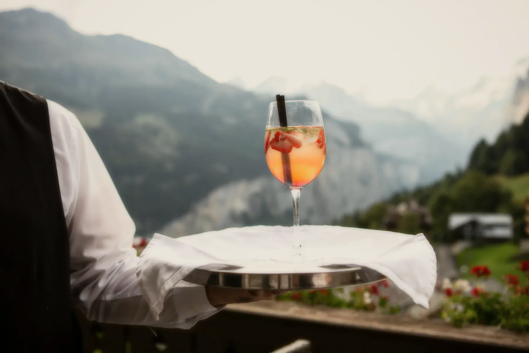 A waiter's tray with a spritz, mountains behind.