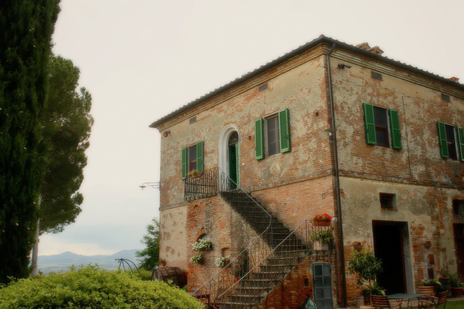 A brick farmhouse with green shutters and an outside stair.