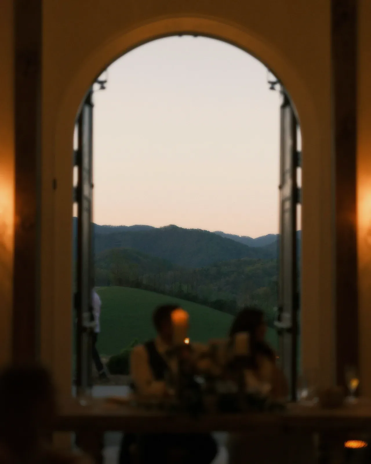 An arched window at dusk over a candlelit dinner.