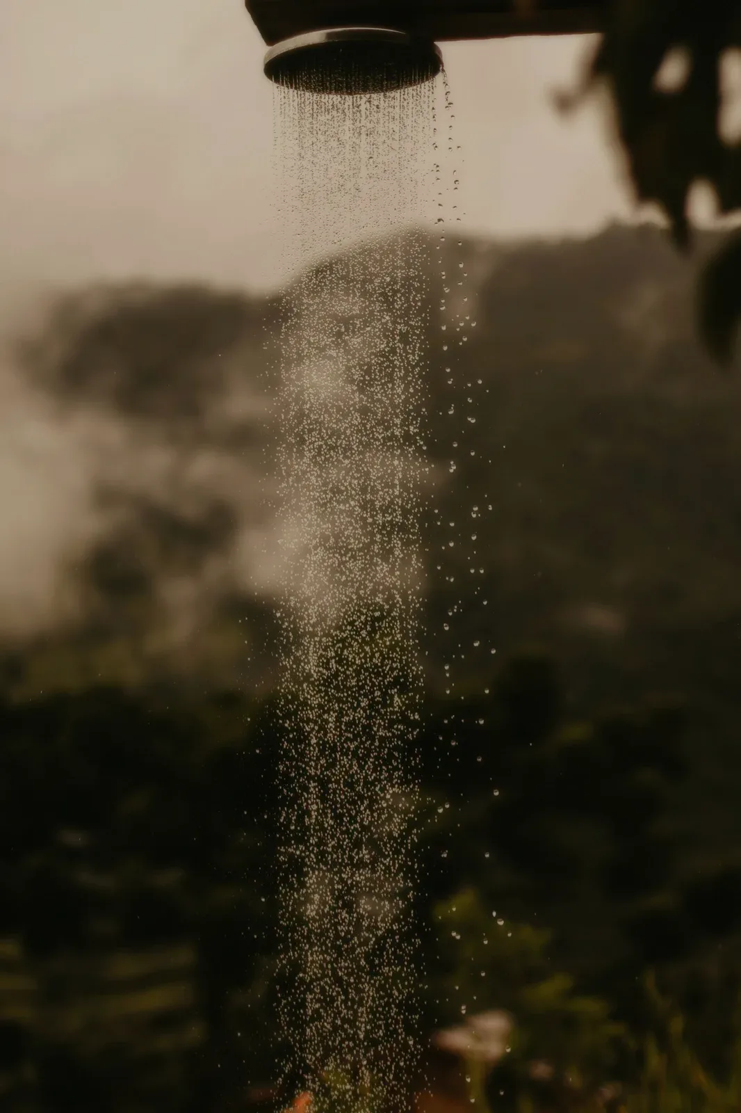 An outdoor shower head, water falling against the hills.