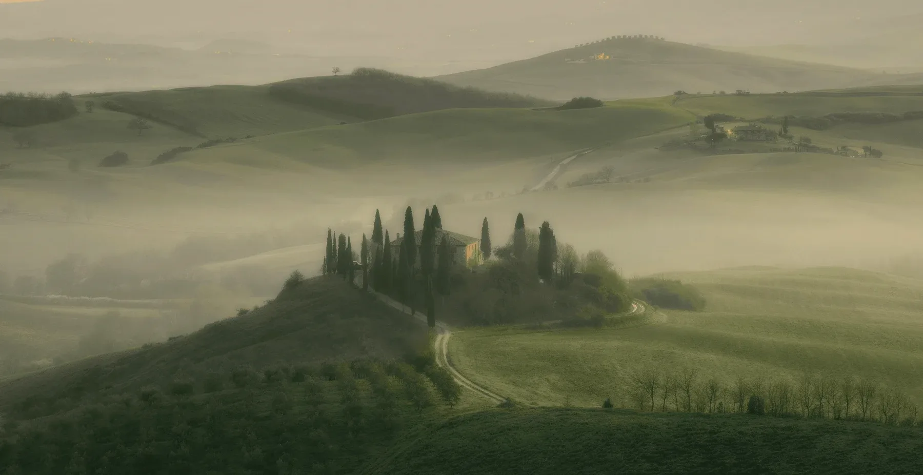 Tuscan hills in morning mist, a villa among cypress trees.