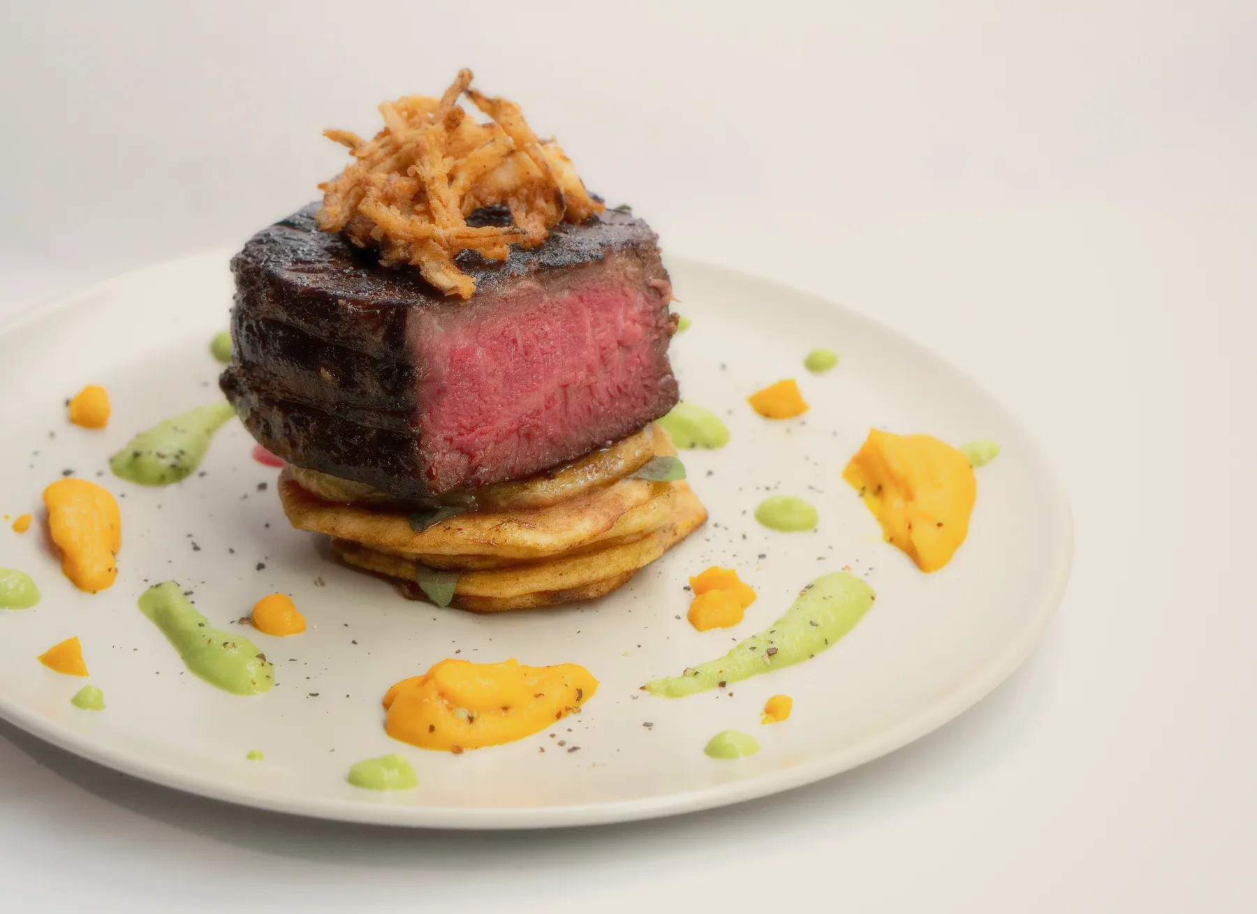 A seared fillet on a white plate with dots of sauce.