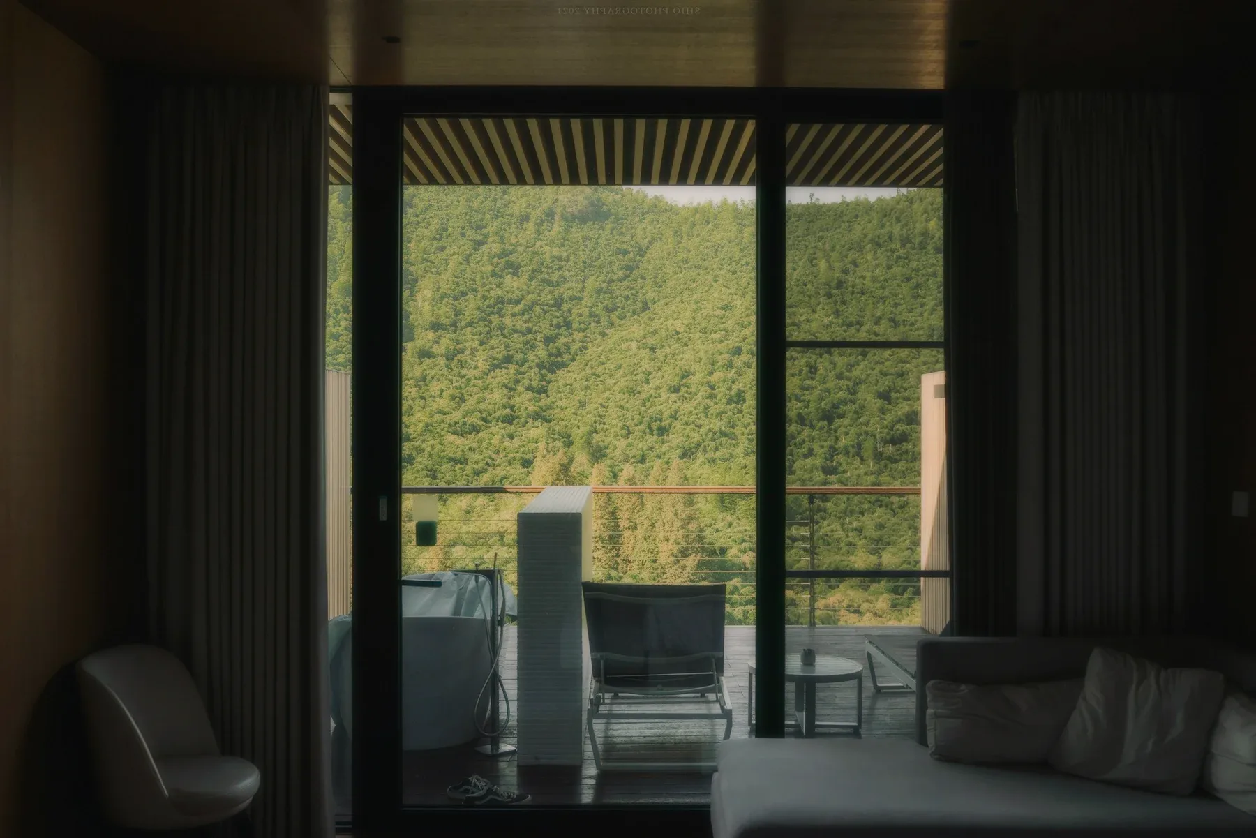 A room open to a terrace, wooded hills beyond the glass.