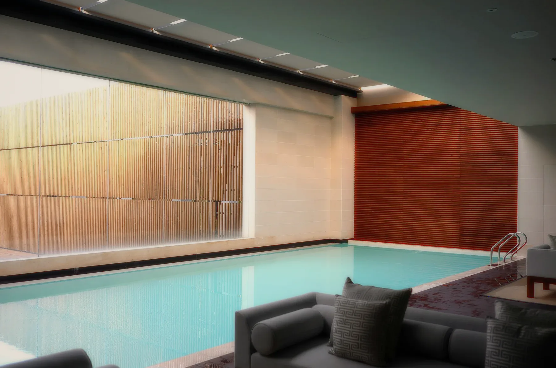 An indoor pool with wooden slats and a grey sofa.