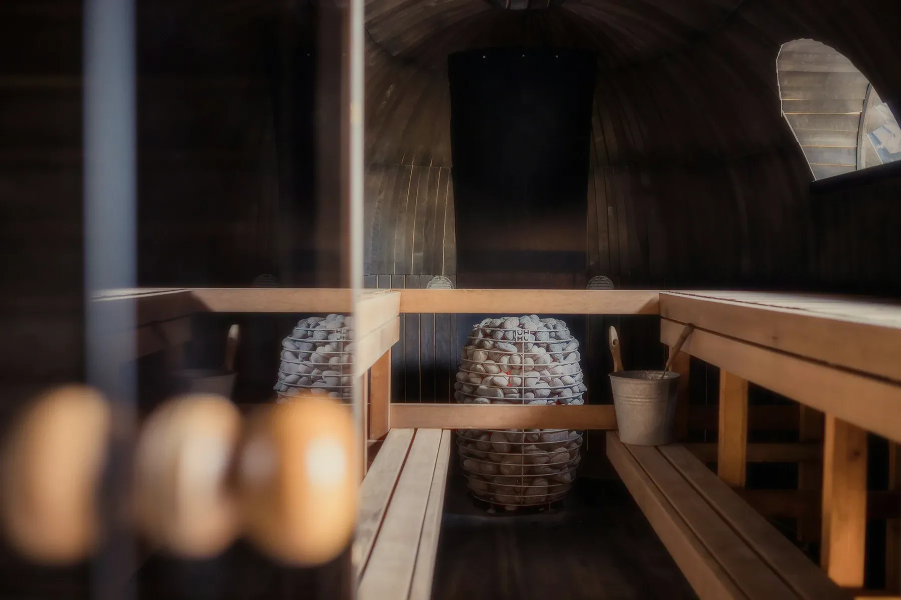 A wooden sauna with a bucket and a basket of stones.