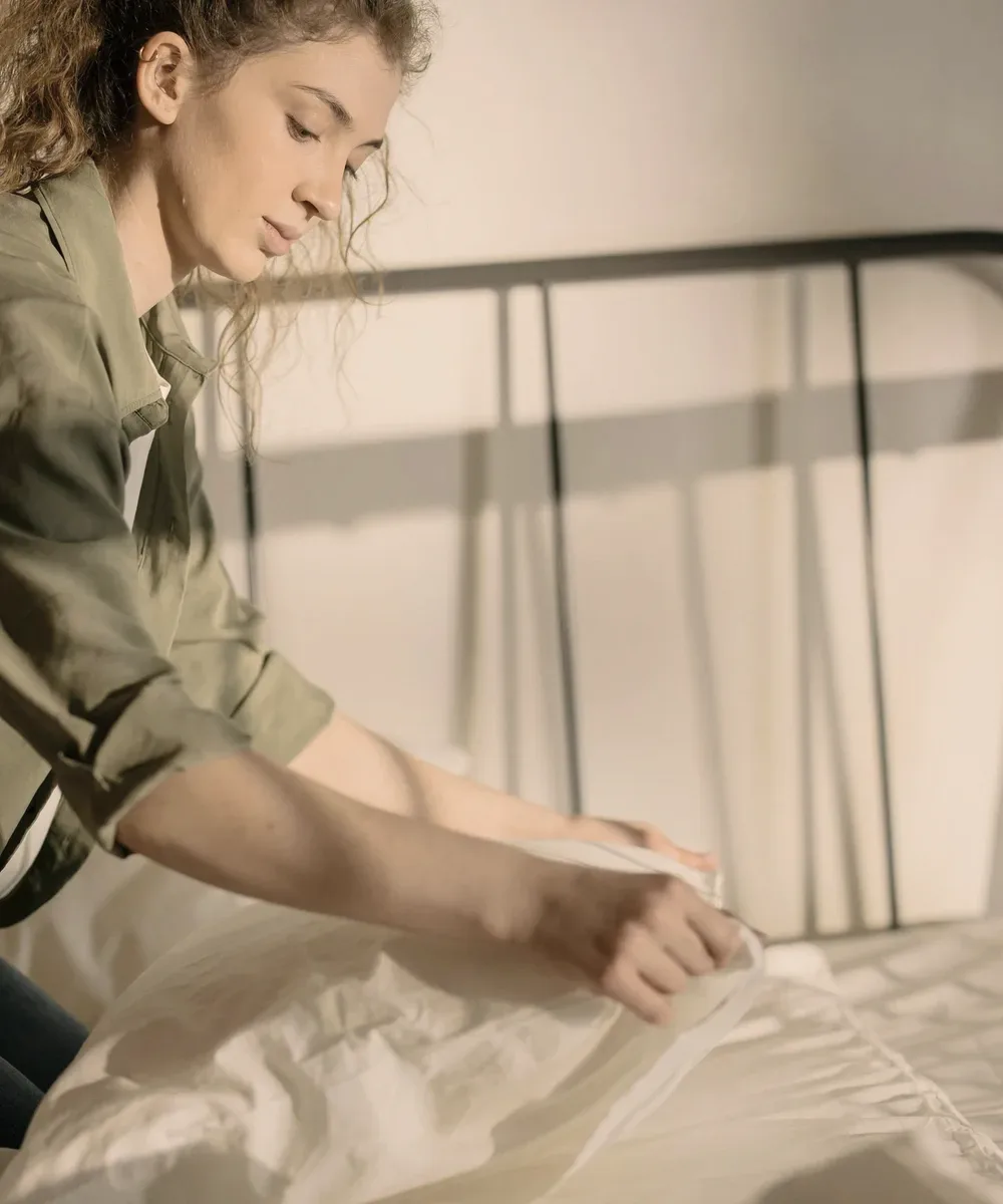 A person folding a sheet on a bed.